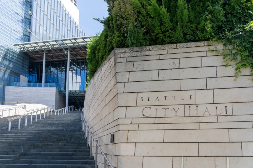 Close-up of engraved stone Seattle City Hall sign in front of wide steps leading to modern glass building.